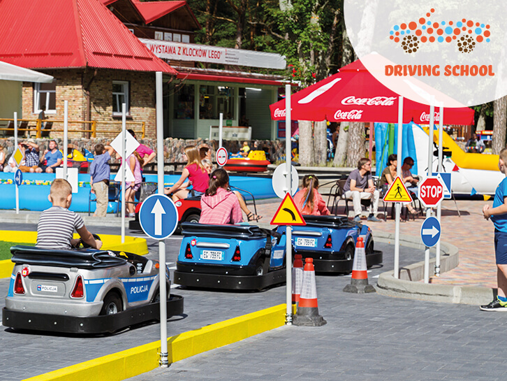 Radosne dzieci jadą samochodzikami po torze Wakacyjnej Szkoły Nauki Jazdy w Discovery Park